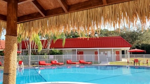 A swimming pool with red lounge chairs and a covered area with a wooden ceiling. - Vero Beach Inn & Suites I-95 (Vero Beach)