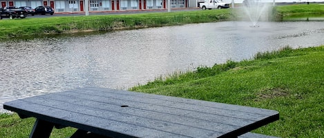 A motel with a red roof, a fountain, and a picnic table in front.