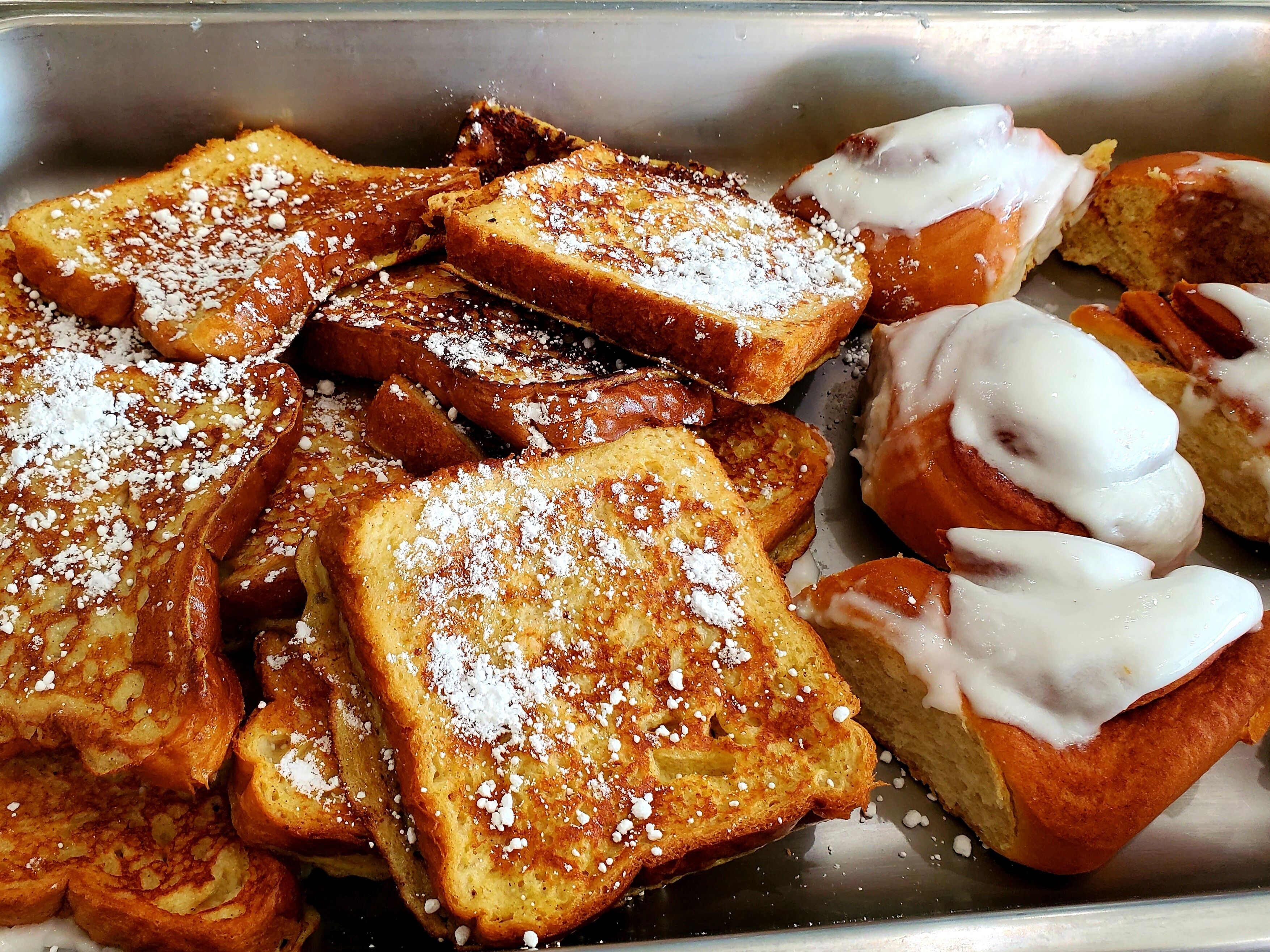 A tray of French toast with powdered sugar and a few pieces of bread with white icing.