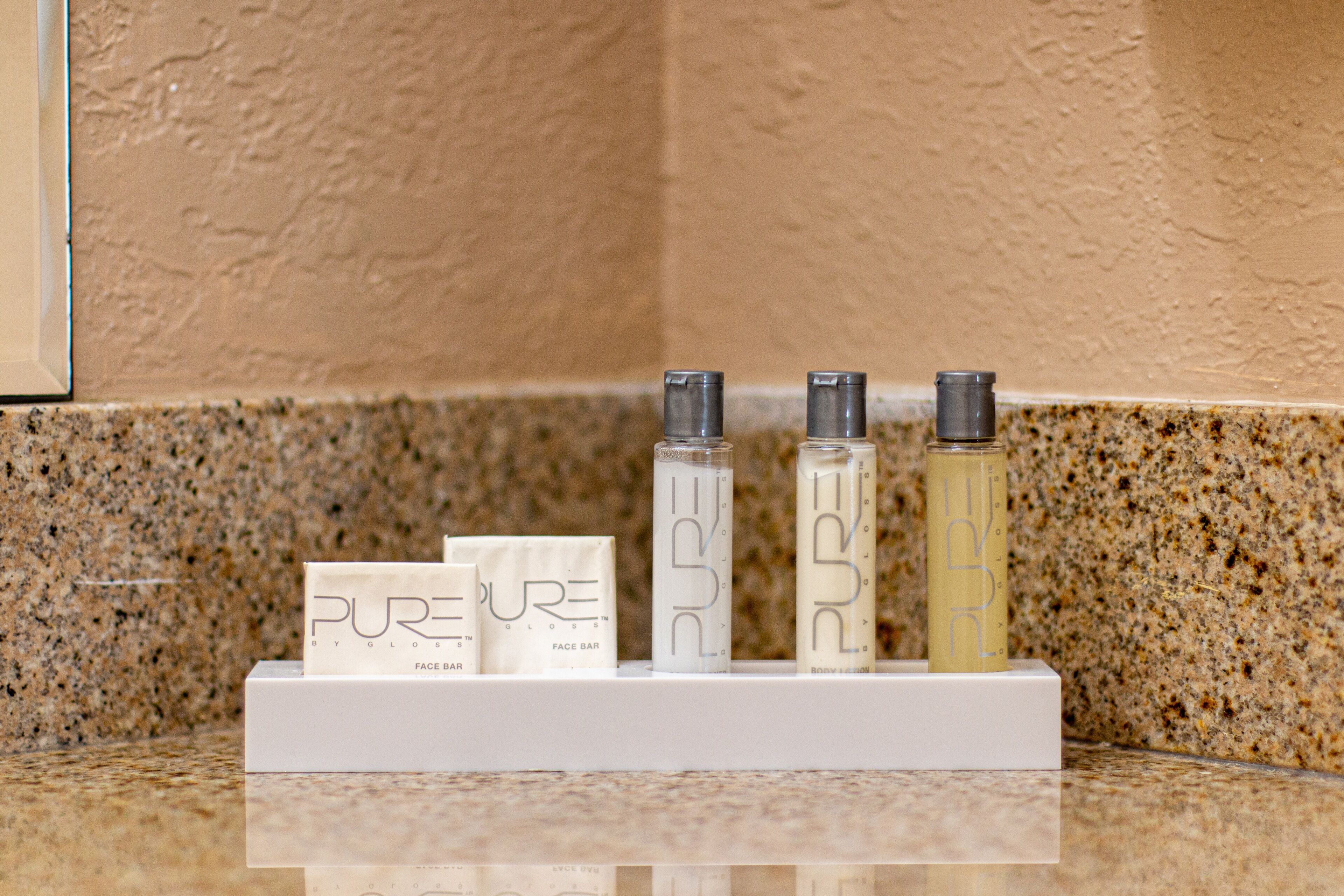A display of PURE brand face and body care products on a white stand against a speckled granite countertop.
