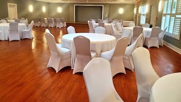 A conference room with round tables and white chairs, wooden floors, and large windows.