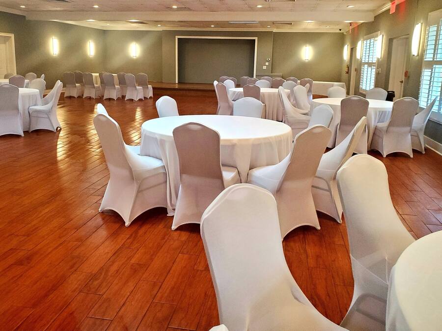 A conference room with round tables and white chairs, wooden floors, and large windows.