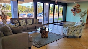 A lobby with a sofa, armchairs, a coffee table, and a large window with a view of parked cars outside. - Vero Beach Inn & Suites I-95 (Vero Beach)