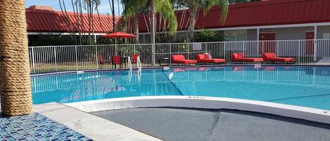 A swimming pool with red lounge chairs and a tiled deck.