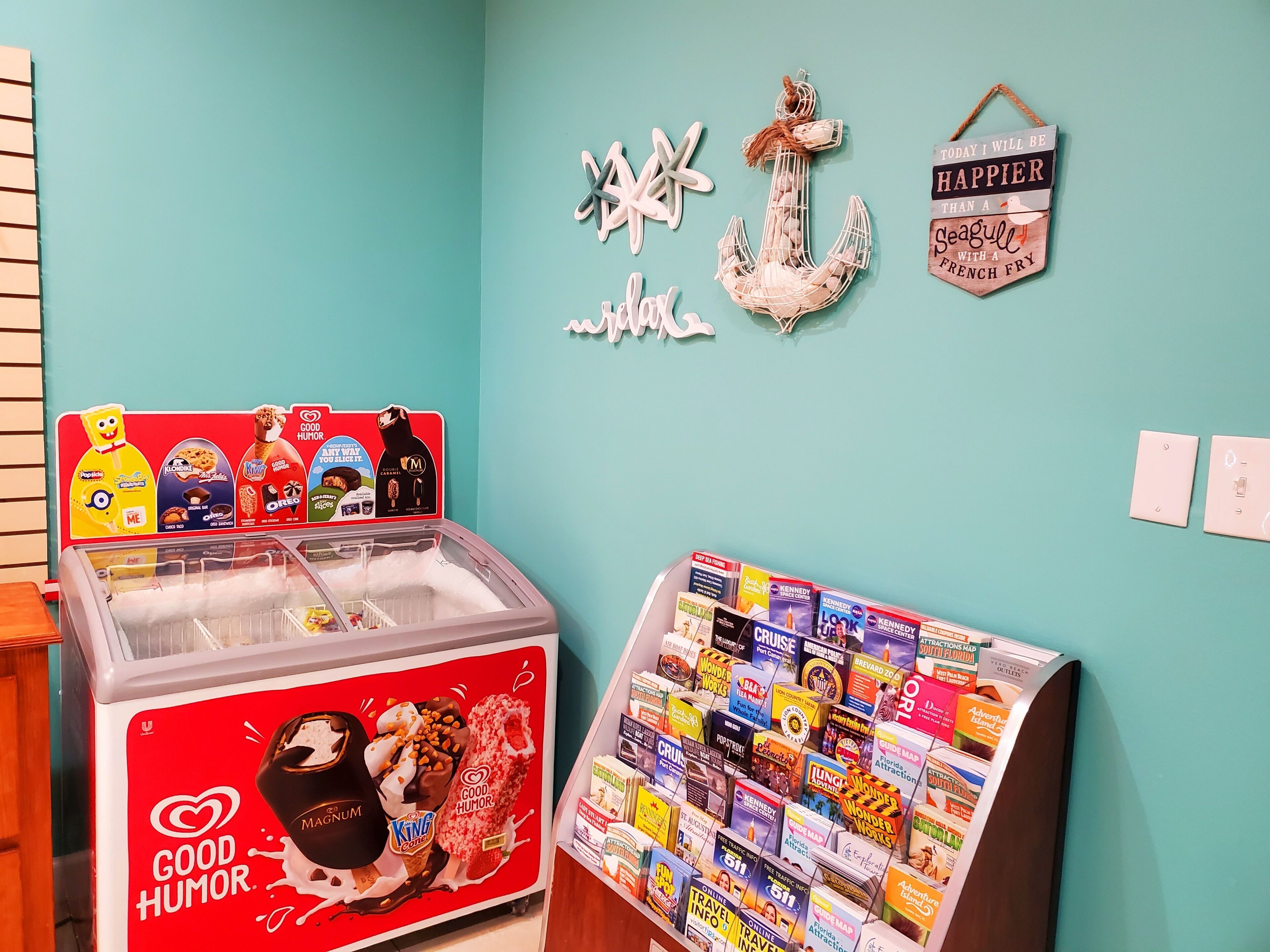 A room with a red ice cream freezer, a wall with a nautical anchor decoration, and a rack of travel magazines.