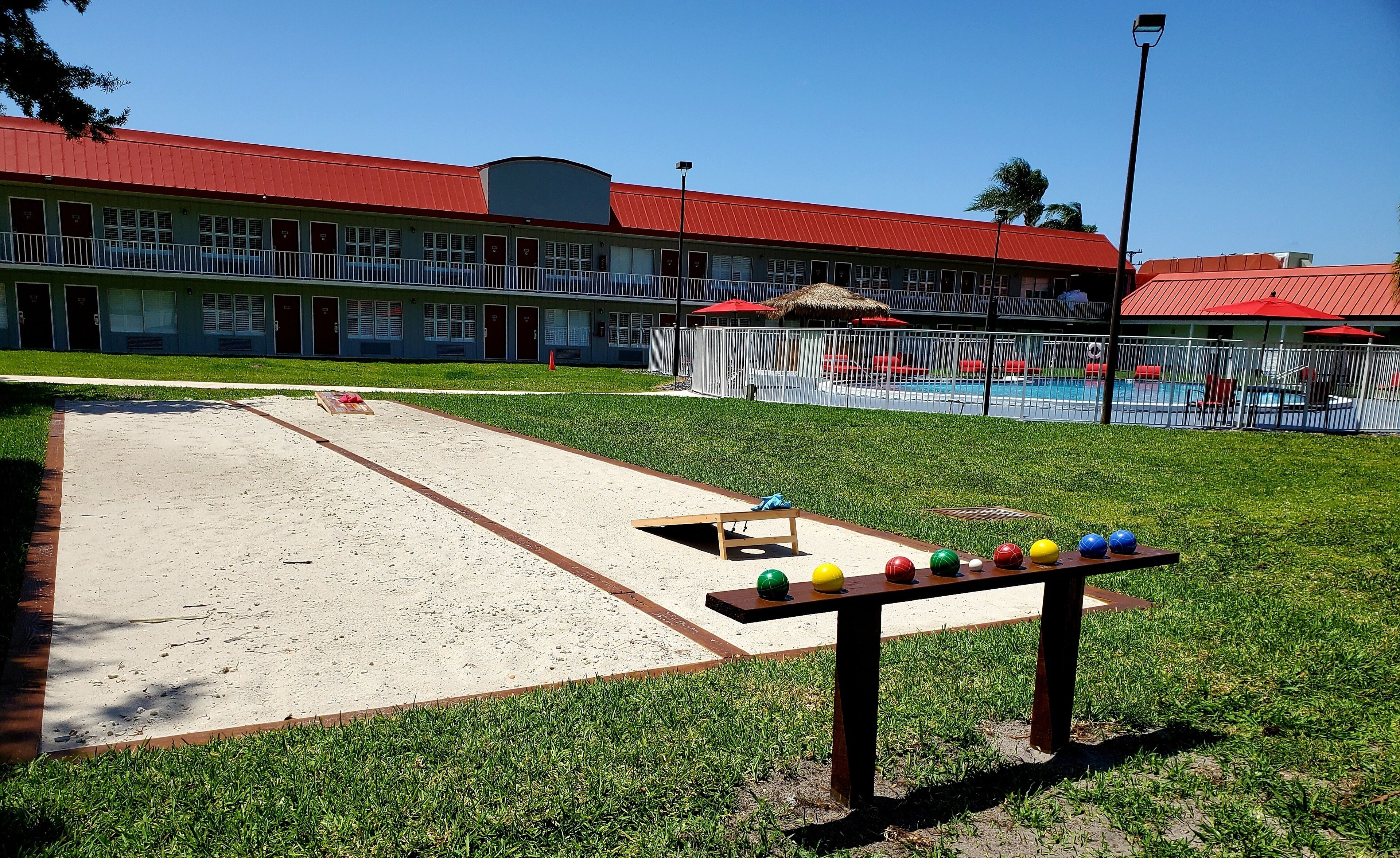 A courtyard with a croquet field, a pool, and a building with red roofs.