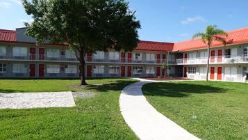 Un motel à deux étages avec des portes rouges et des balcons, un arbre au centre et un chemin pavé.