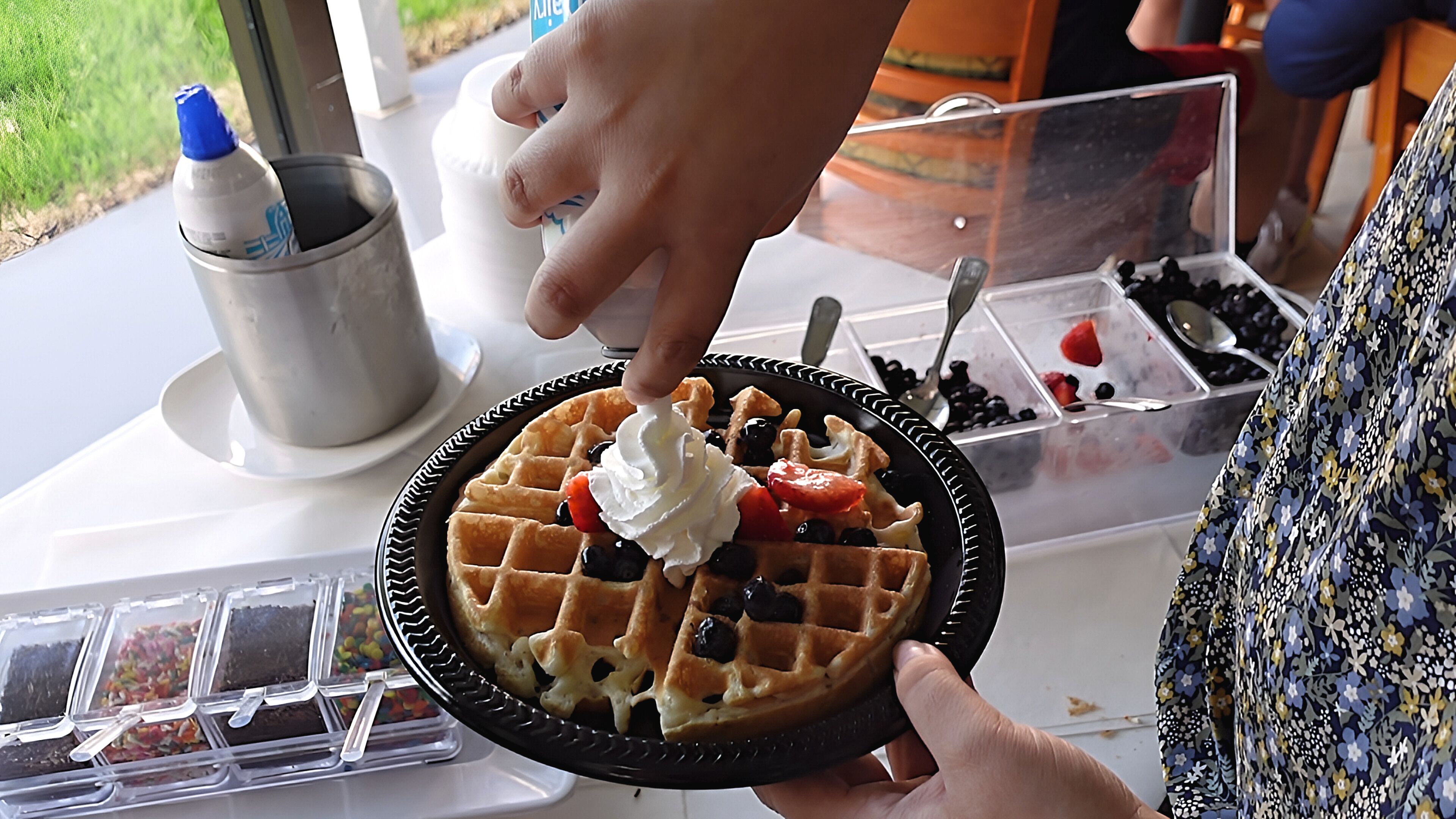 Una persona aguantant un waffle amb nata i fruita a sobre.