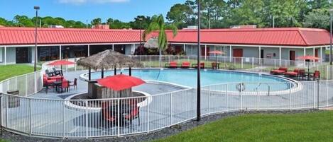 A pool area with a fenced deck, lounge chairs, and umbrellas.