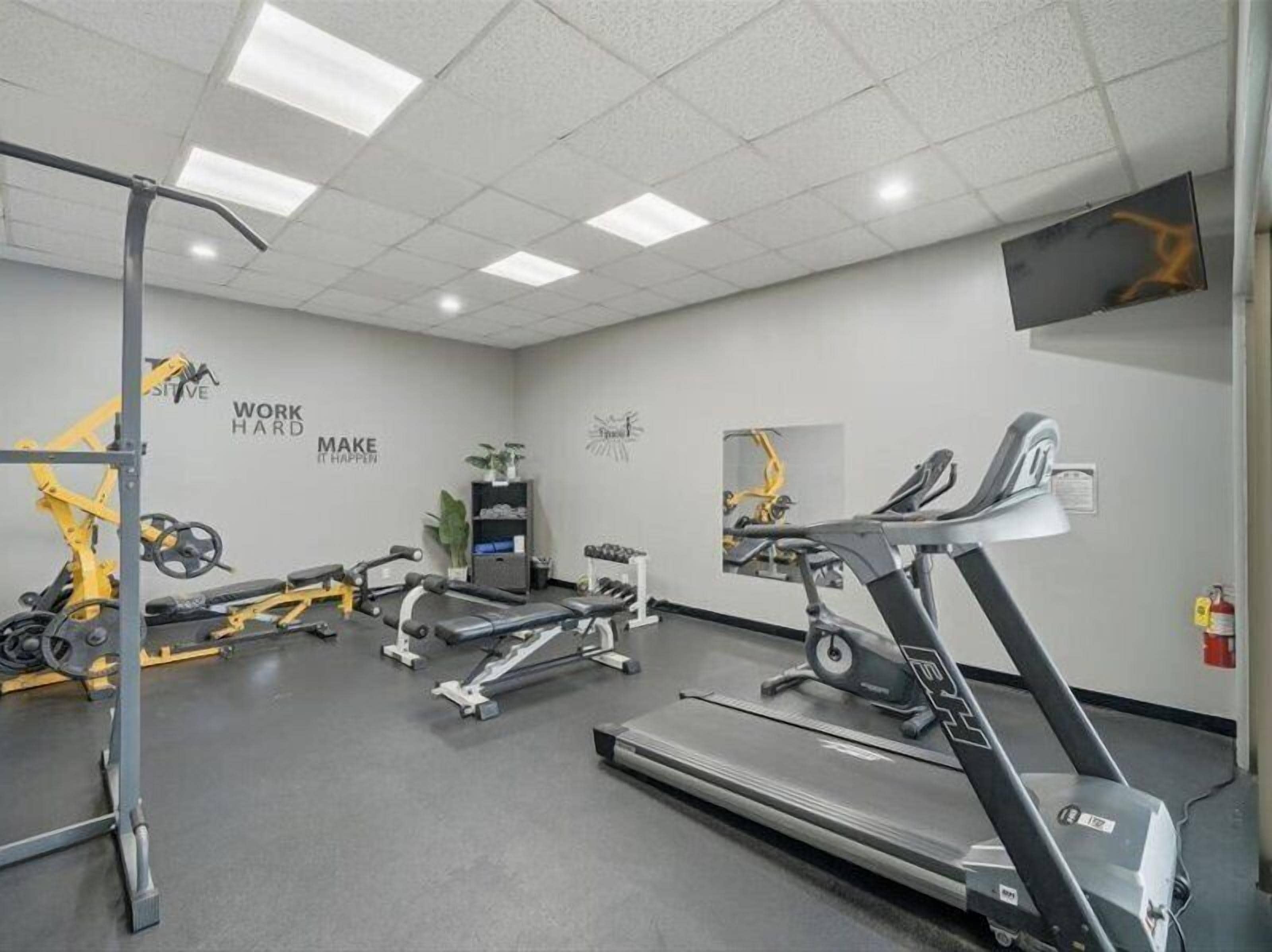 Une salle de sport équipée de matériel d’exercice, agrémentée de décorations murales inspirantes et dotée d’un téléviseur à écran plat.