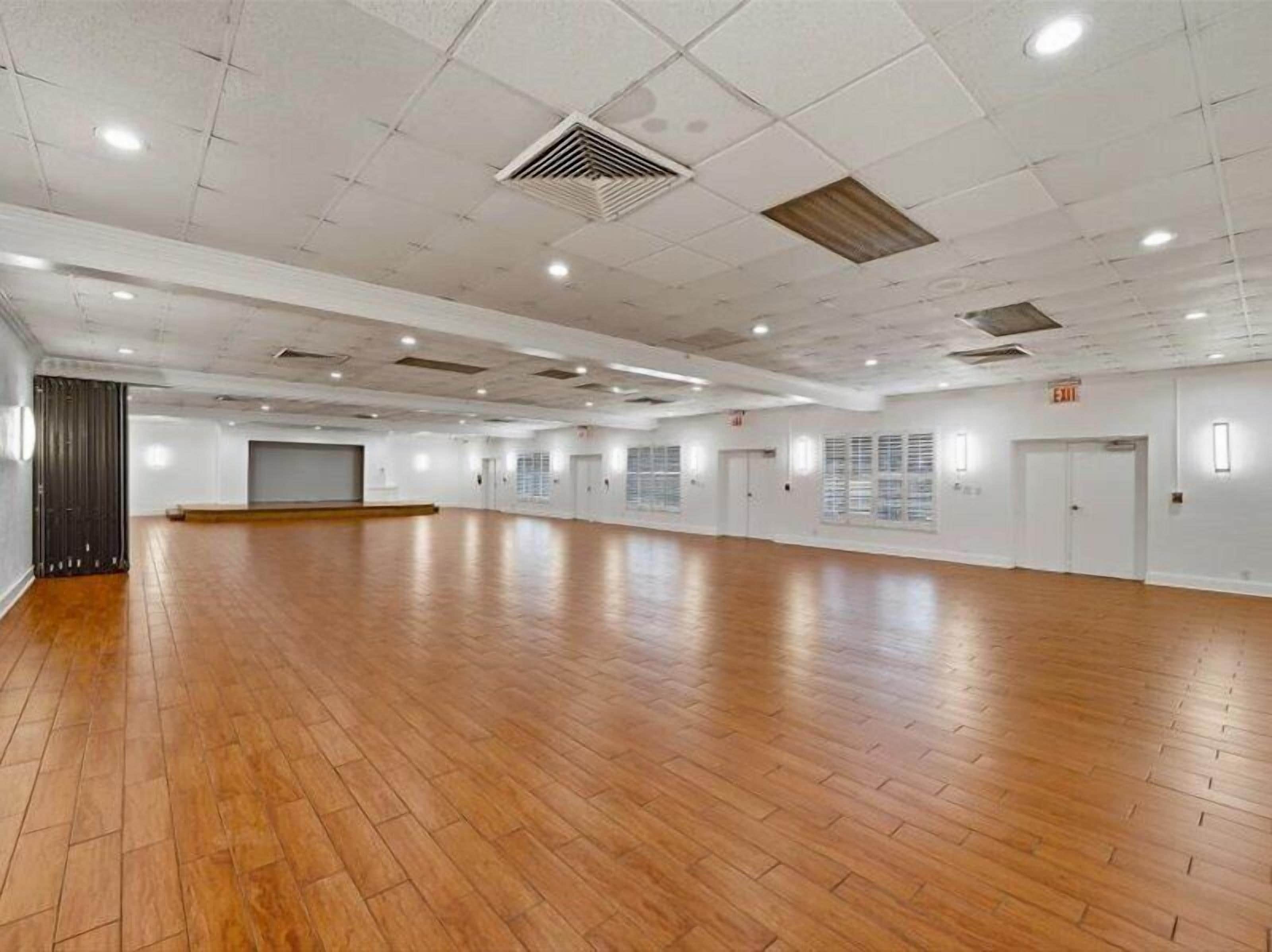 A large, empty room with wooden flooring, white walls, and multiple doors.