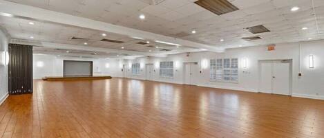 A large, empty room with wooden flooring, white walls, and multiple doors.