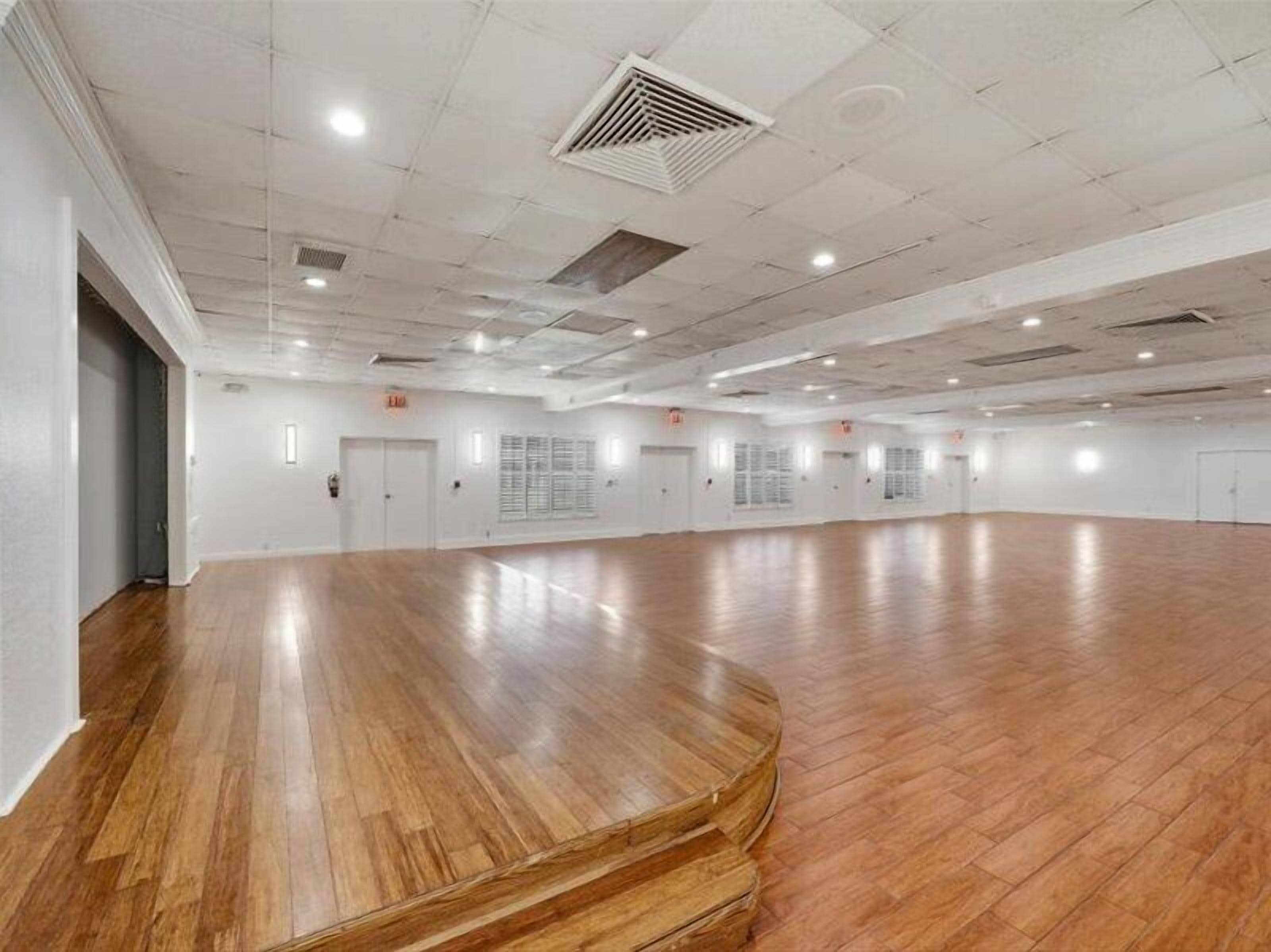 Un espacio amplio y abierto con piso de madera pulida, paredes blancas y un techo alto con iluminación empotrada.