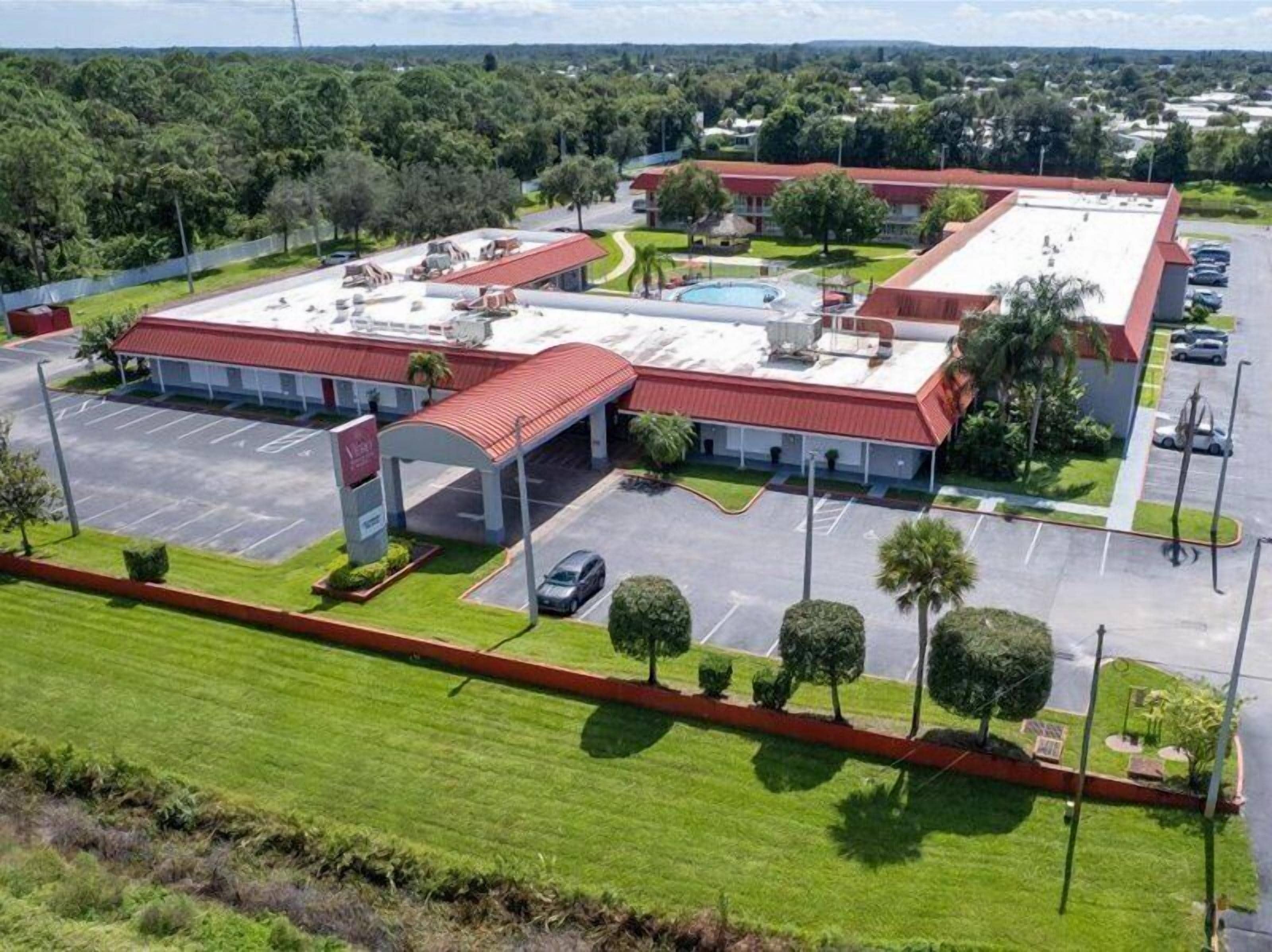 A large building with a red roof, a parking lot, and a swimming pool.