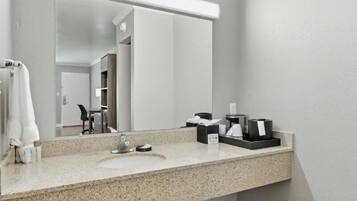 A hotel bathroom with a granite countertop, a sink, a mirror, and a towel rack.