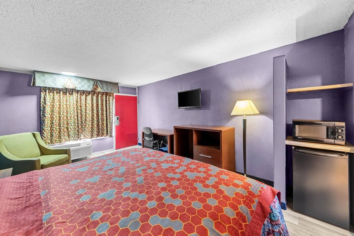 A hotel room with a bed, a desk, a chair, a television, a microwave, and a refrigerator.