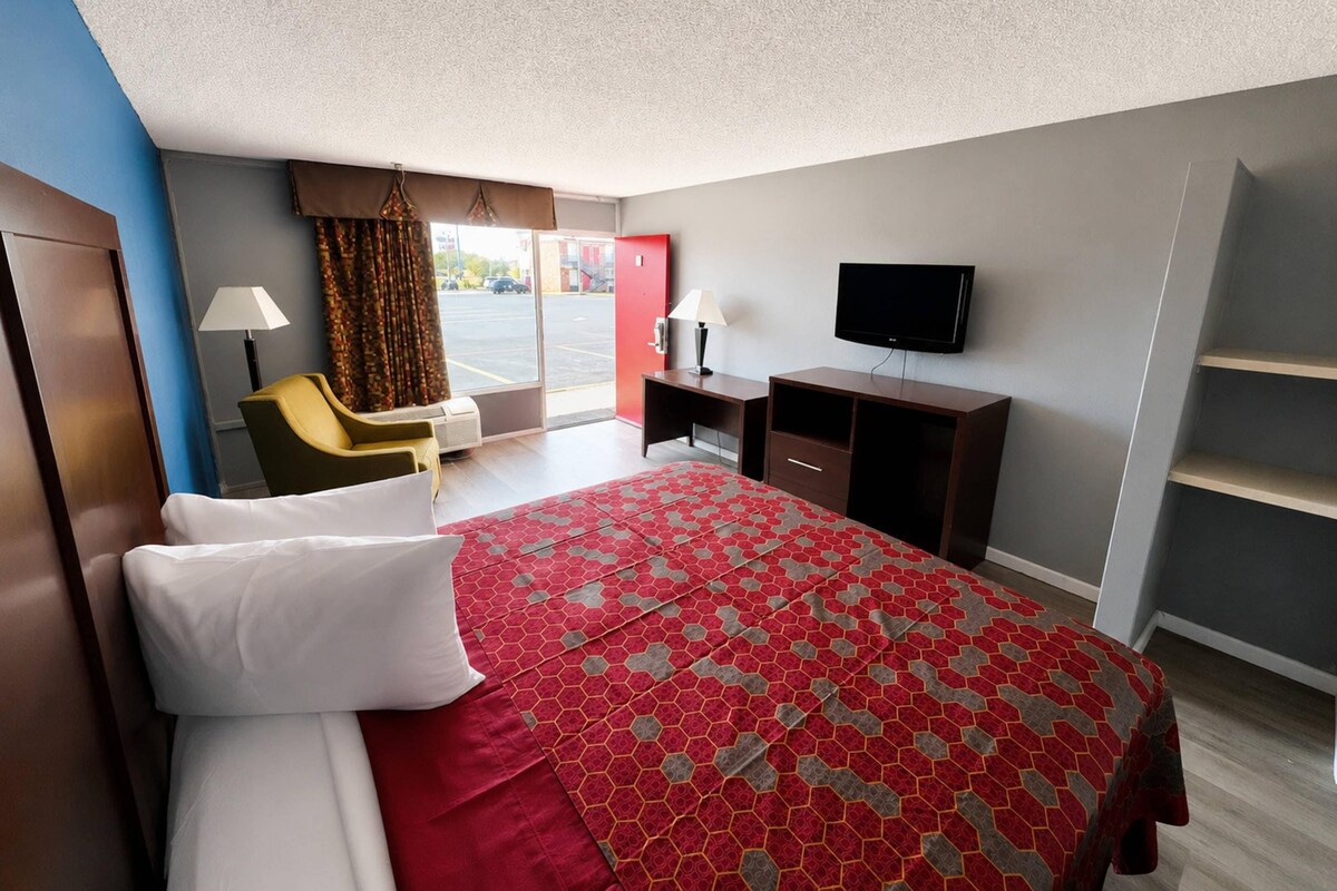 Habitación de hotel con cama, escritorio, silla, televisión y vista al exterior.