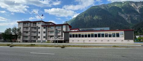 A multi-story hotel with balconies, a parking lot, and a mountain backdrop.