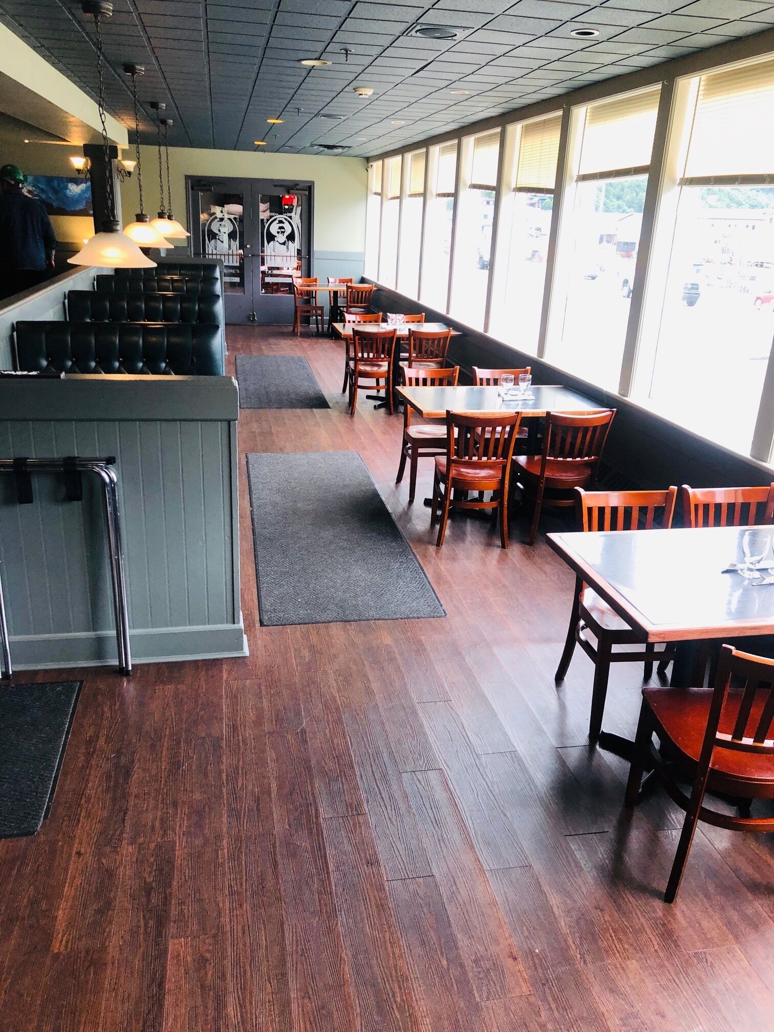 A restaurant interior with wooden flooring, tables, and chairs. There is a counter with a menu and a person in the background.
