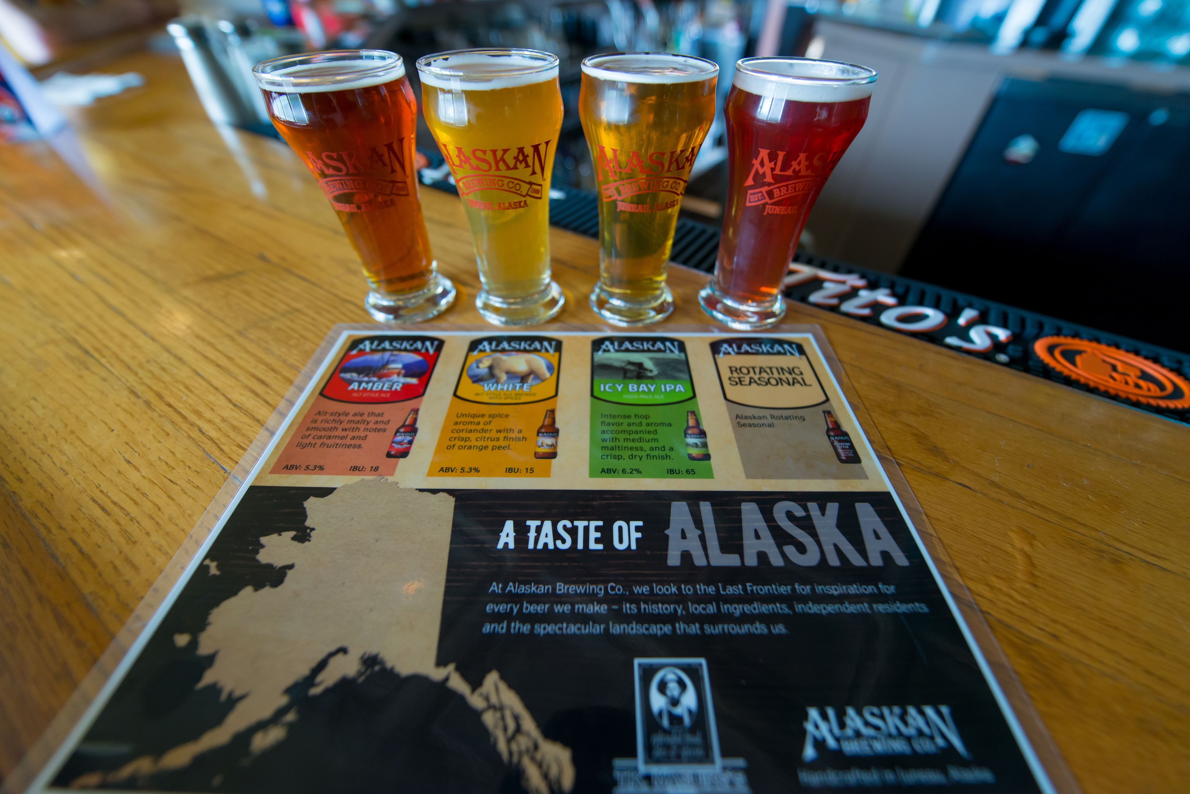 A bar with four glasses of beer labeled "Alaskan" and a menu detailing different beer types.