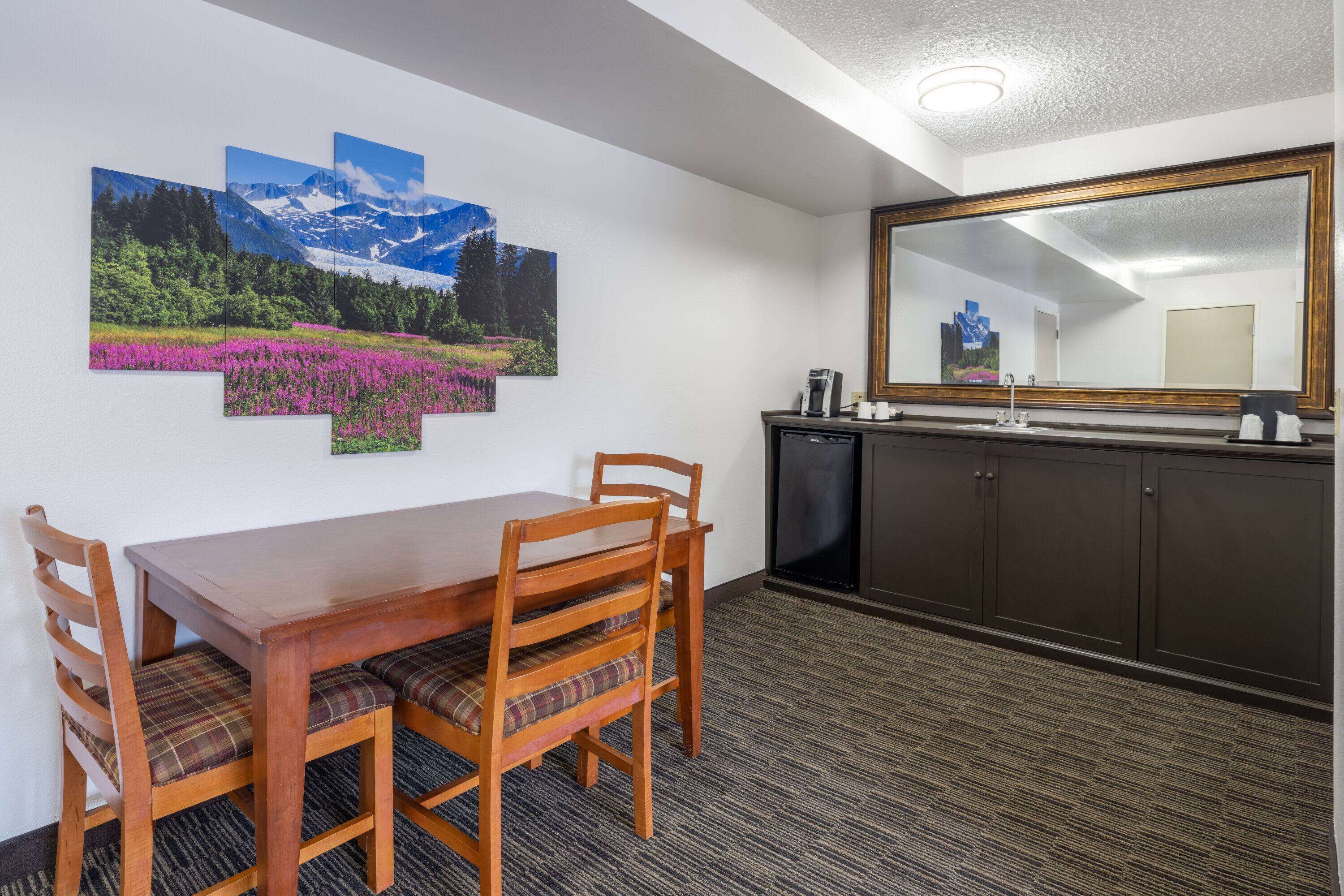Habitación de hotel con una mesa de comedor, sillas, un espejo grande y una obra de arte en la pared que muestra un paisaje montañoso.