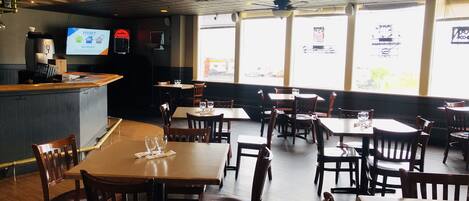 A restaurant interior with wooden tables and chairs, a counter with a menu display, and large windows allowing natural light.