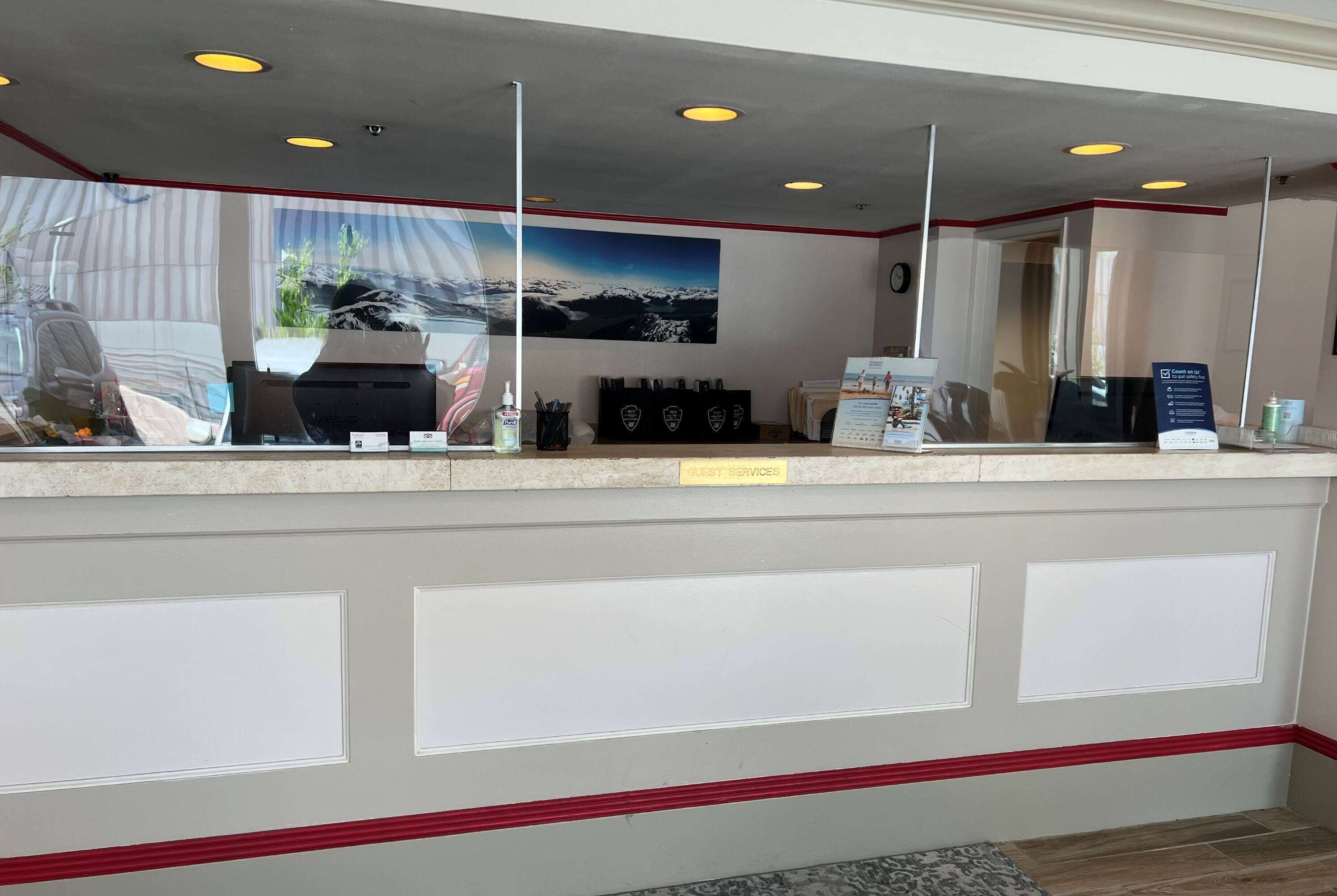 A reception desk with a glass partition, a mounted security camera, and a "Guest Services" sign.