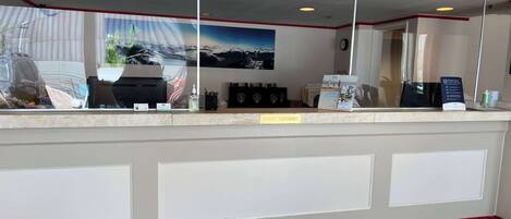 A reception desk with a glass partition, a mounted security camera, and a "Guest Services" sign.