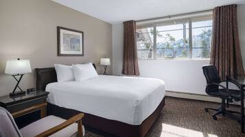 Habitación de hotel con una cama grande, dos mesitas de noche con lámparas, una silla, un escritorio y una ventana con cortinas.