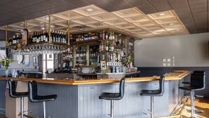 A bar area with a bar counter, multiple stools, and a variety of bottles and glasses on shelves. - Ramada by Wyndham Juneau (Juneau)