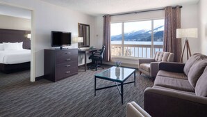 A hotel room with a bed, desk, TV, and a view of mountains through the window. - Ramada by Wyndham Juneau (Juneau)