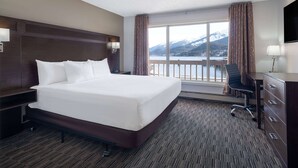 A hotel room with a large bed, a desk, a chair, a TV, and a view of mountains and a lake. - Ramada by Wyndham Juneau (Juneau)
