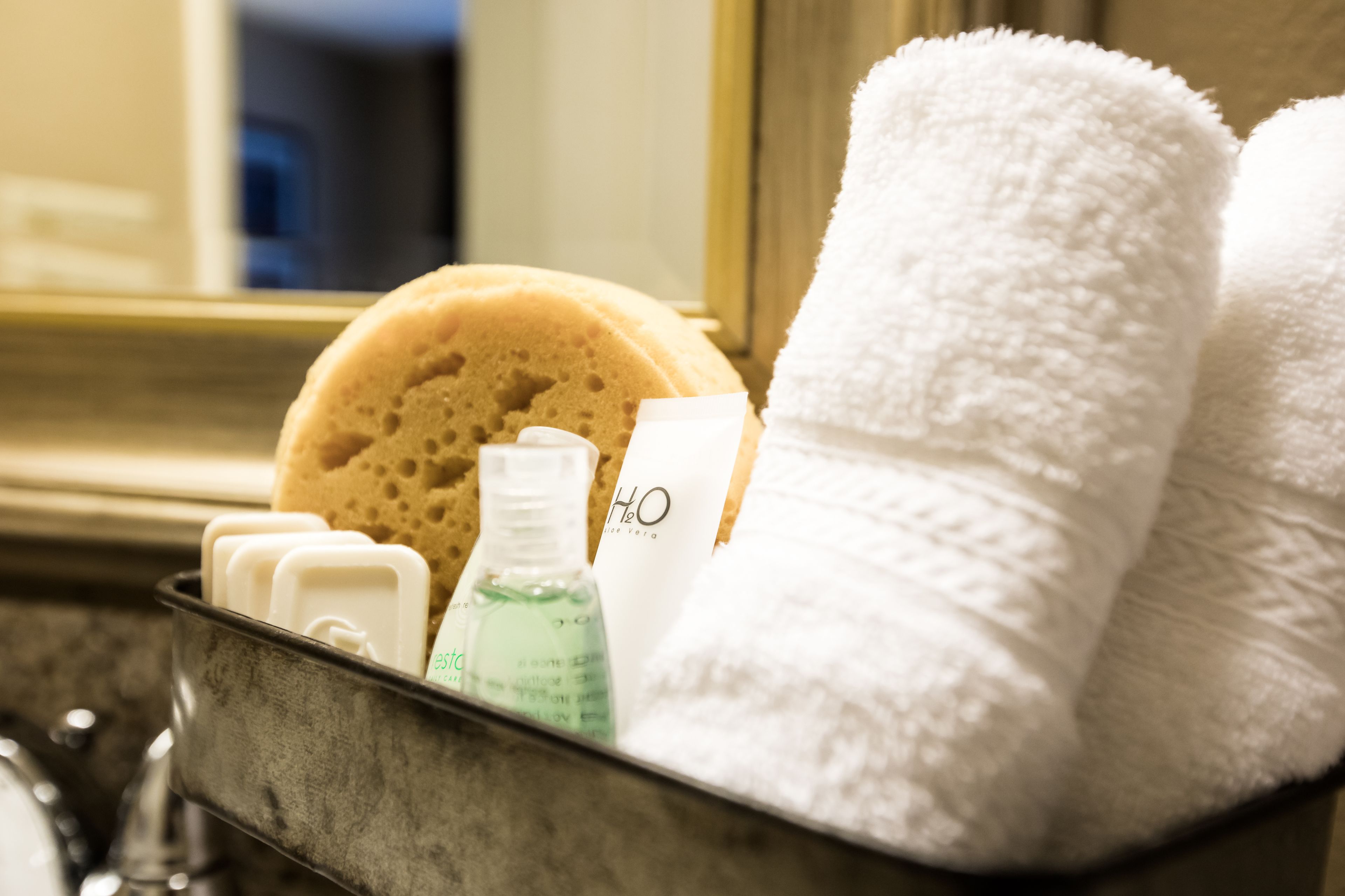 A bathroom with a bathtub, a towel rack with two white towels, a bottle of liquid soap, and a sponge.