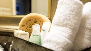 A bathroom with a bathtub, a towel rack with two white towels, a bottle of liquid soap, and a sponge.