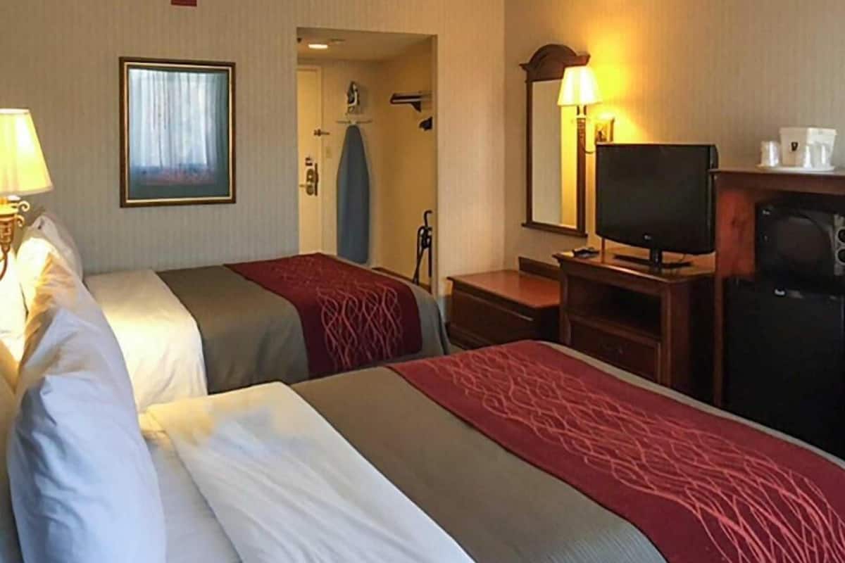 A hotel room with two beds, a television, a desk, and a mirror.