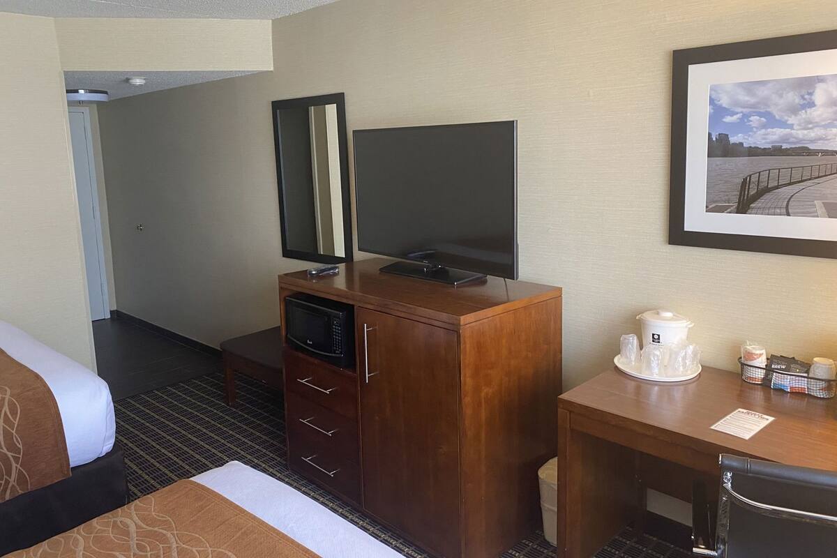 A hotel room with a bed, a wooden desk with a coffee maker, a television, and a framed picture on the wall.