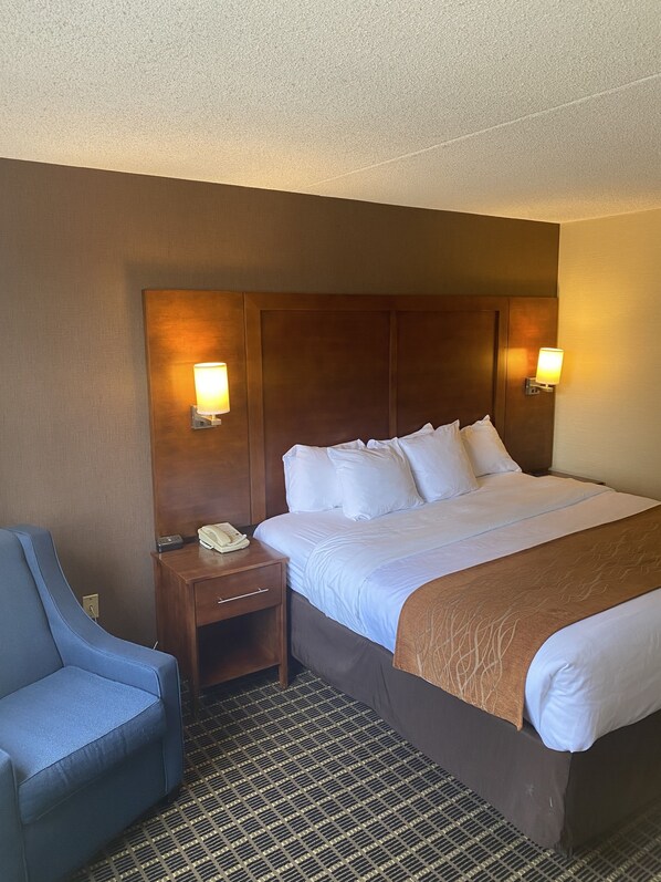 A hotel room with a bed, two bedside lamps, a desk with a telephone, and a blue chair.