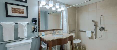 A bathroom with a sink, mirror, shower, and toilet. There are towels hanging on the wall and a small stool.