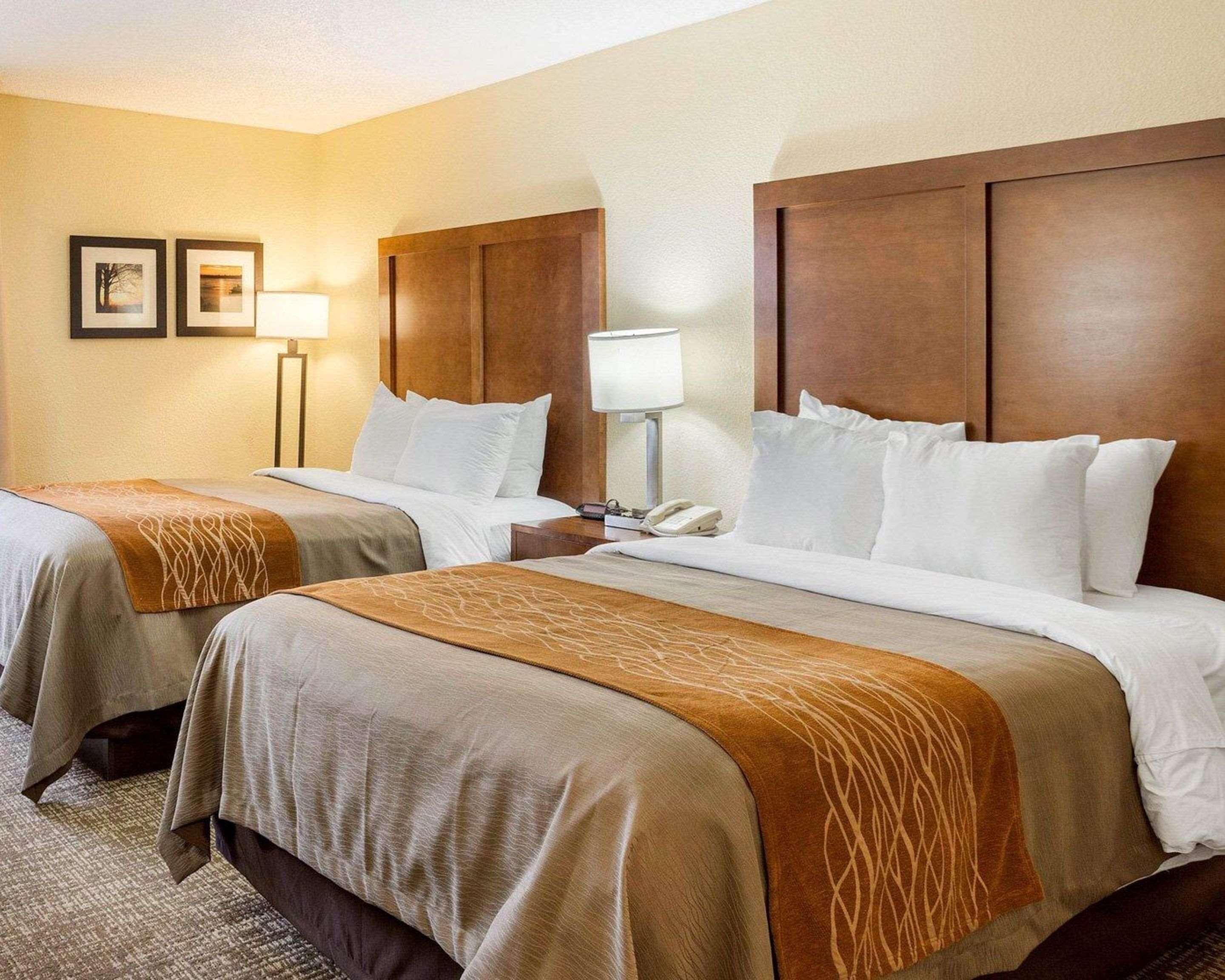 A hotel room with two beds, each with a headboard, bedside tables, lamps, and a phone.
