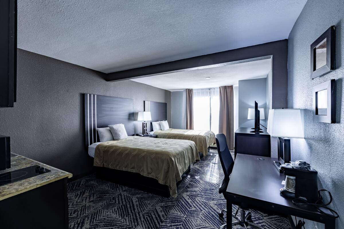 Ein Hotelzimmer mit zwei Betten, einem Schreibtisch, einem Stuhl, einem Fernseher und einer Lampe.