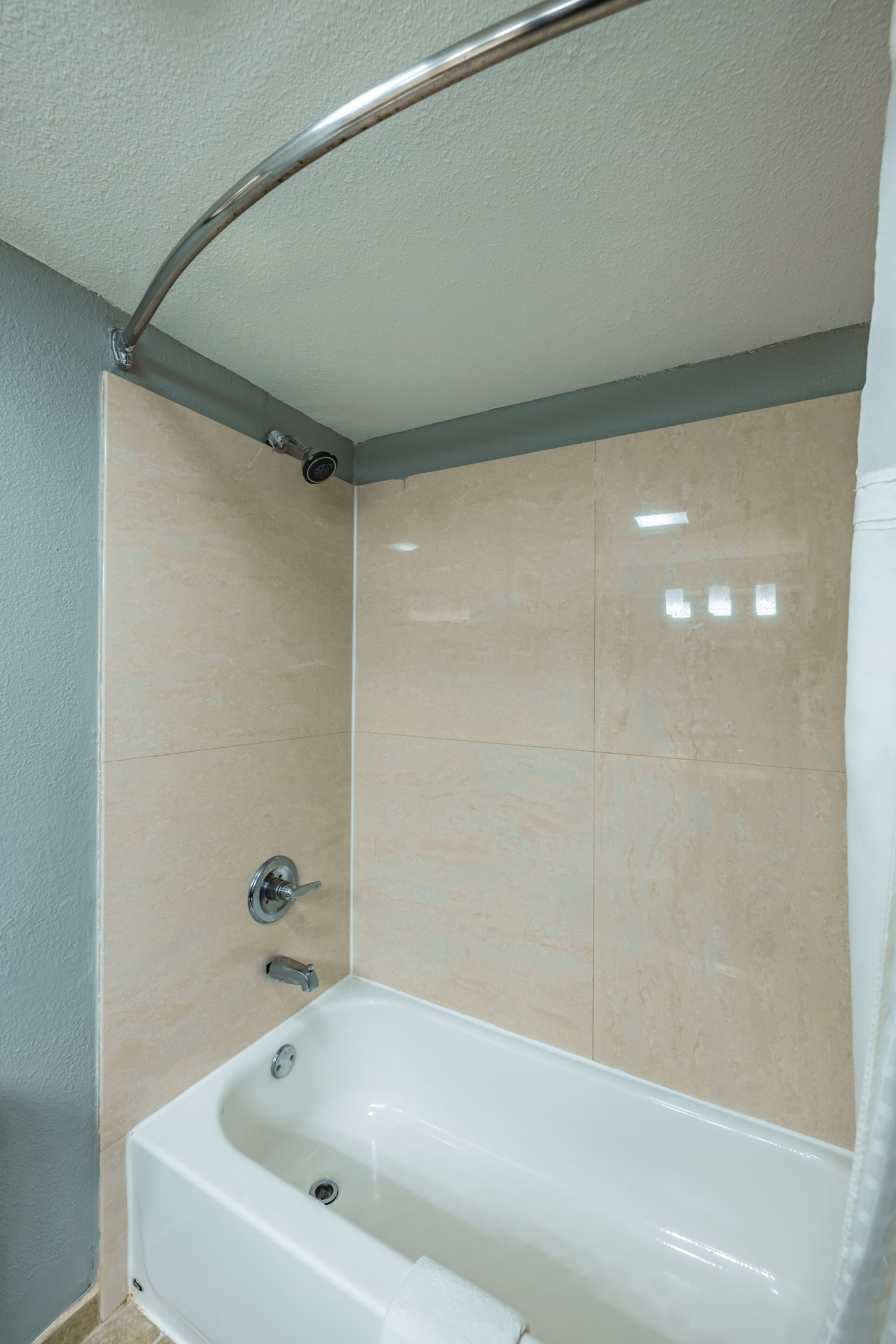 A bathroom with a bathtub, a shower area, and a corner with a curved metal fixture.
