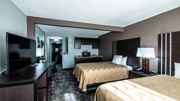 A hotel room with a bed, a desk with a TV, a bedside table with a lamp, and a bathroom visible through an open door.