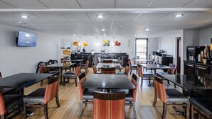 Un restaurante con varias mesas y sillas, una zona de cocina y un televisor en la pared.