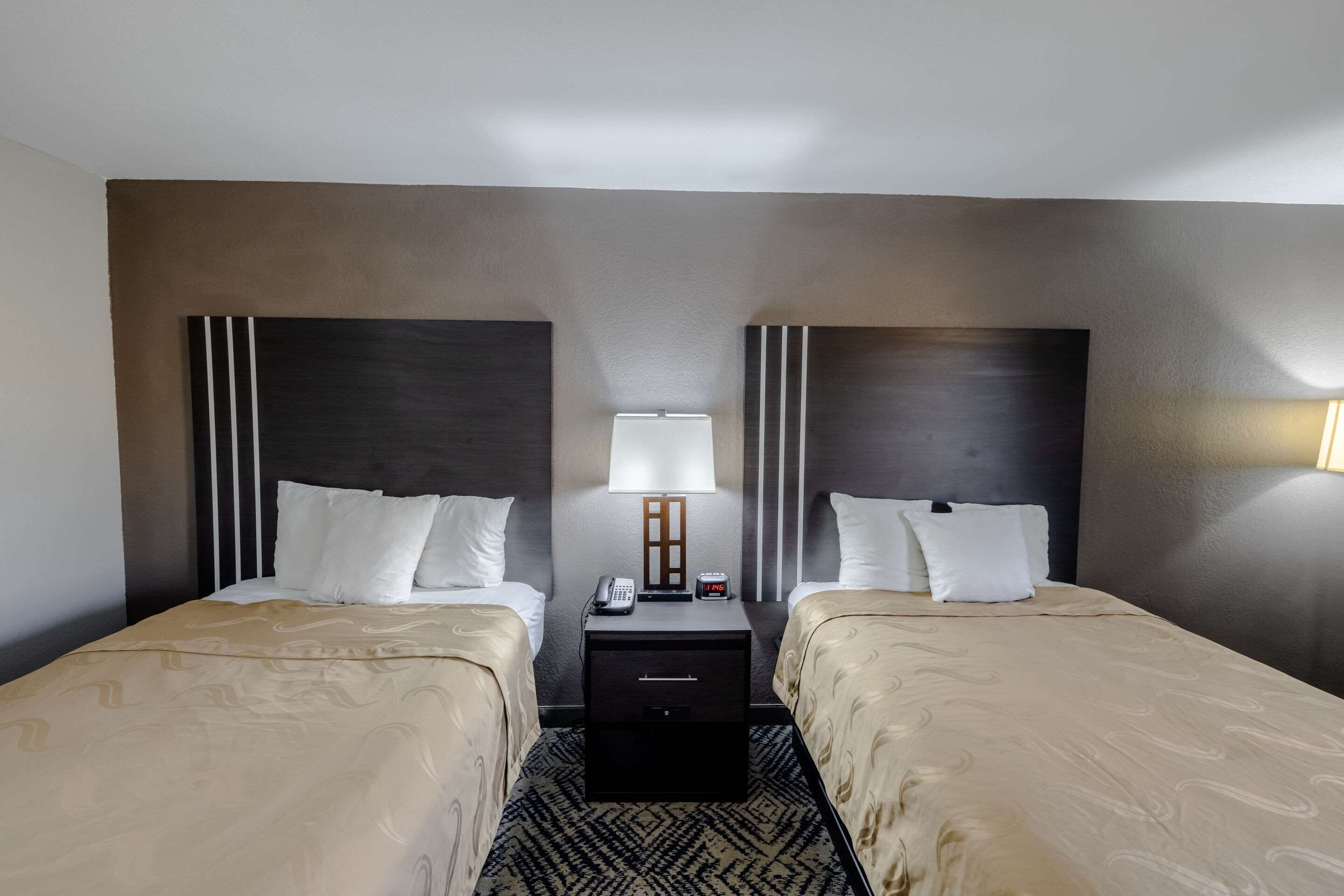 A hotel room with two beds, a nightstand with a lamp, and a small drawer.