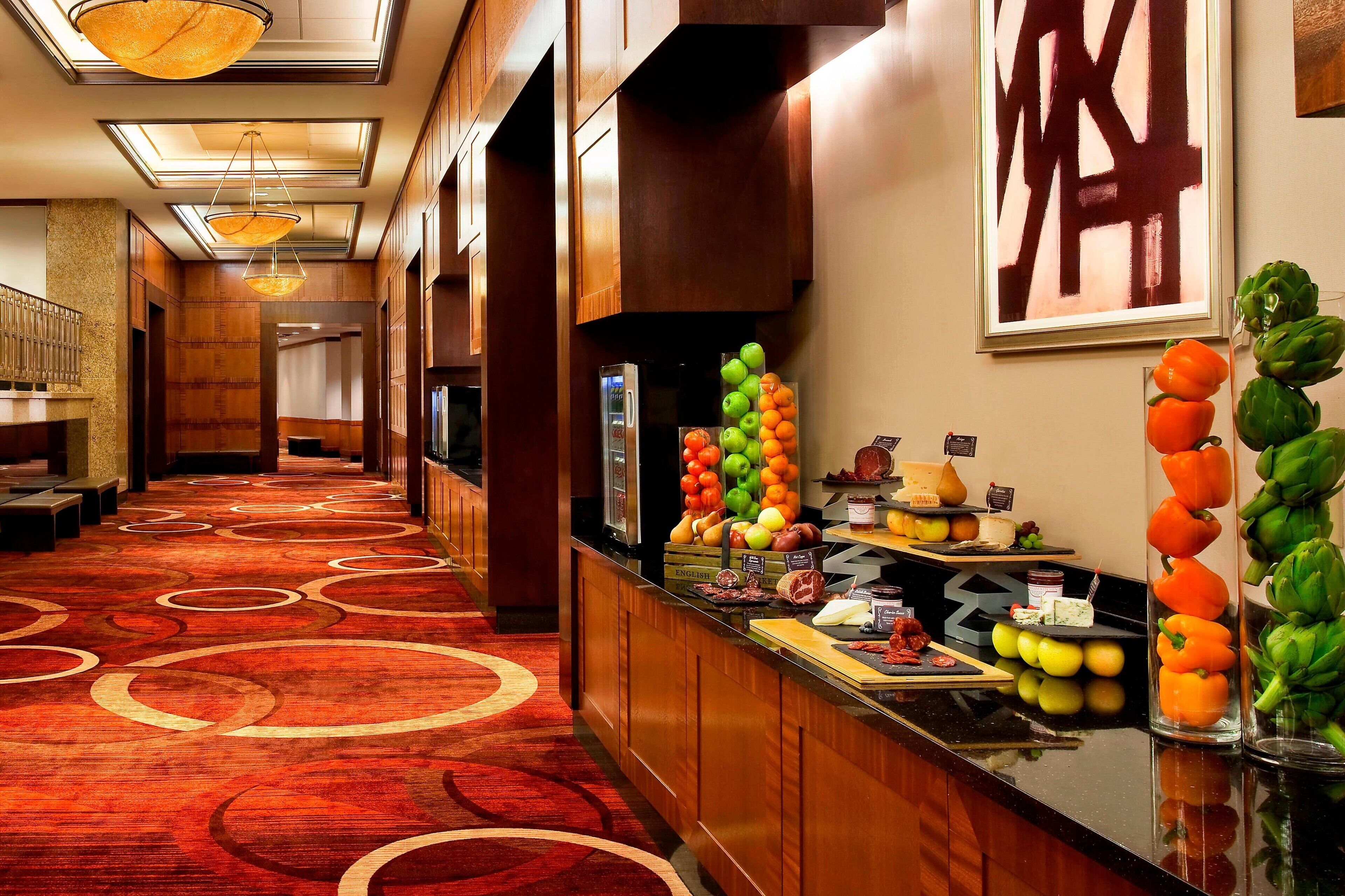 A hotel lobby with a red carpet, a reception desk with fruit and cheese, and a large abstract painting on the wall.