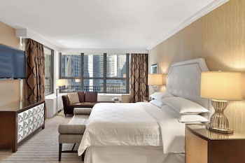 A spacious hotel lobby with a large chandelier, comfortable seating, and a view of the city through large windows. at Sheraton New York Times Square Hotel
