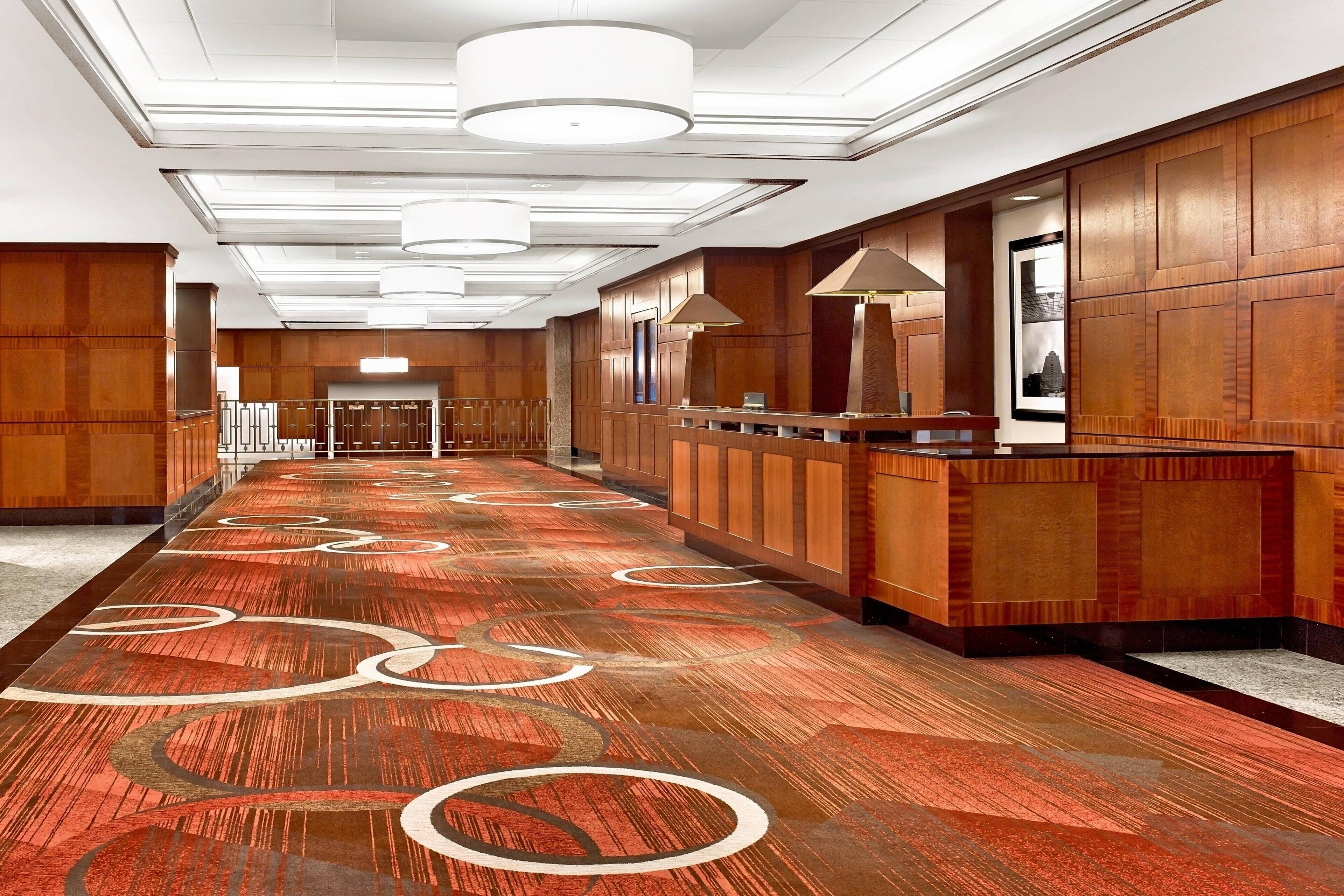A hotel lobby with a long reception desk, wooden paneling, and a patterned carpet.