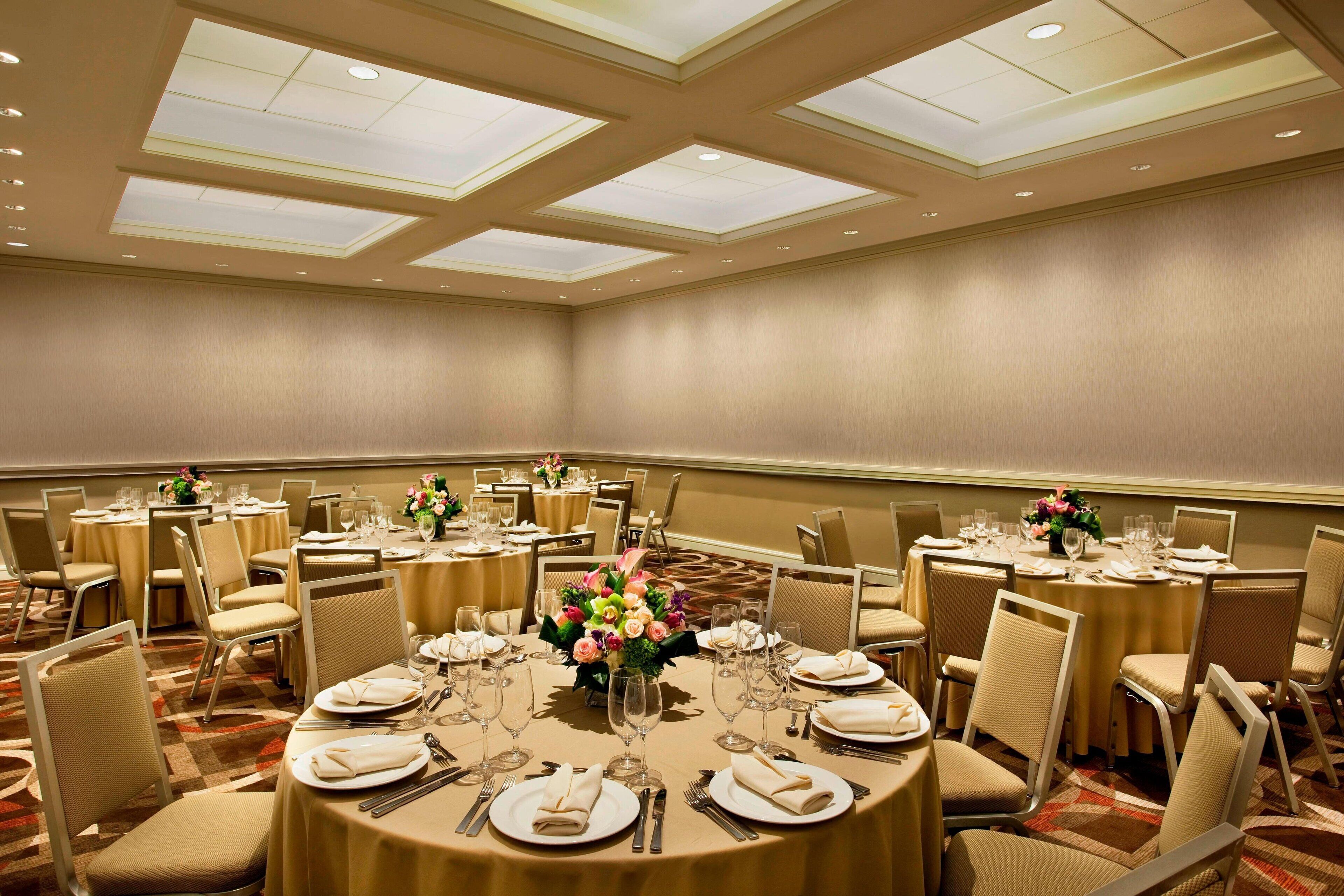 Une salle de conférence avec des tables rondes, des chaises de couleur beige et des arrangements floraux en guise de décoration centrale.