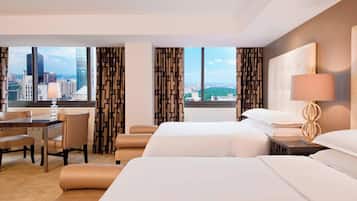 A hotel room with two beds, a desk, and a view of the cityscape.