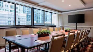 A conference room with a long table, chairs, a TV, and large windows with a city view.
